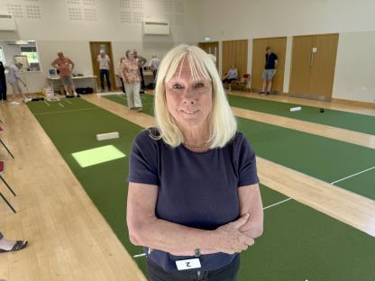 Woman standing in a hall with indoor bowling greens in the background.