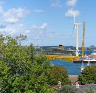 Cruise ship at a seaside town with a wind turbine and construction crane.
