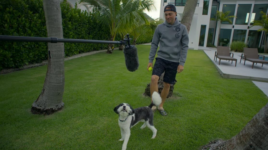 Justin Thomas holding a tennis ball with his dog in his yard.