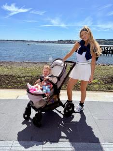 Woman pushing a stroller with a toddler along a waterfront.