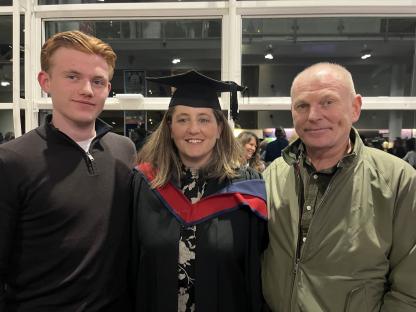 A woman in graduation robes poses for a photo with two other people.
