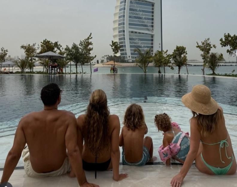 Rio Ferdinand, his wife, and two children sitting poolside looking at the Burj Al Arab hotel in Dubai.