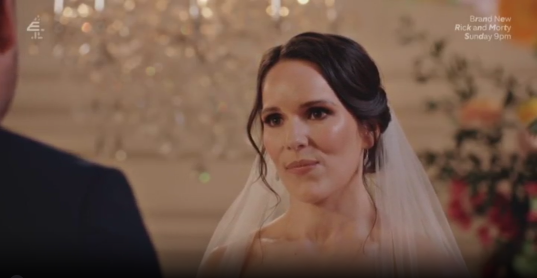 A bride in a white veil looks at her groom.