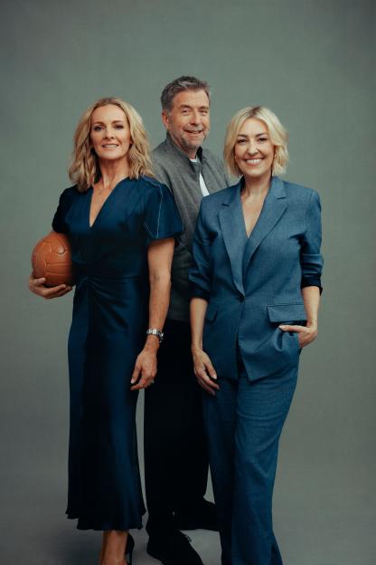 Three people posing for a photo; a woman in a blue dress holding a ball, a man in a gray jacket, and a woman in a blue suit.