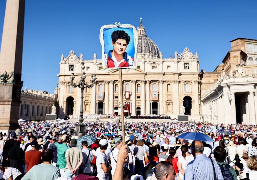 Person holding a portrait of Carlo Acutis at a canonization Mass in St. Peter's Square.