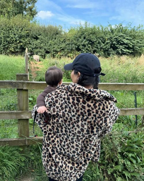Kourtney Kardashian holds her baby while looking at an animal in a field.