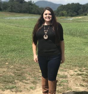 Woman in black top and jeans standing in a field.