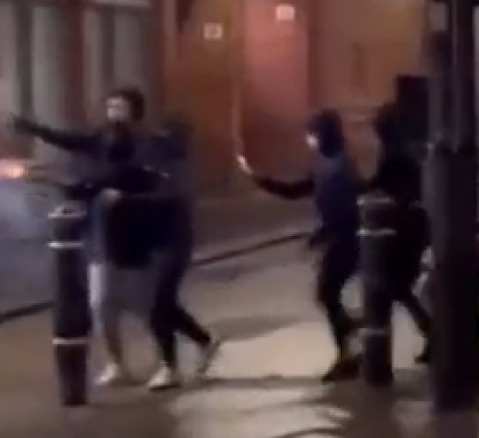 Two people walking on a street, one holding a flare.