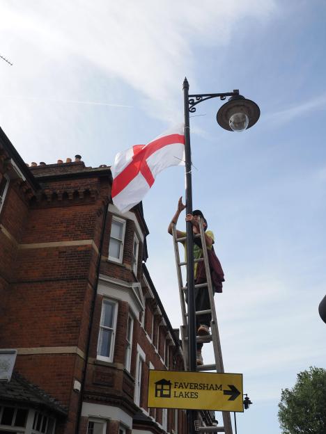 A person on a ladder removing a St George flag from a lamp post in Faversham.