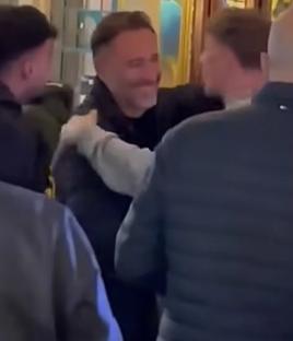 Split image: a man being embraced by two others, and a man in a black jacket with a wolf logo.
