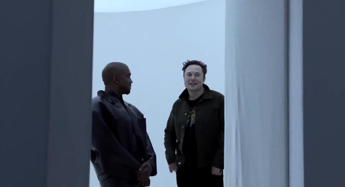 Kanye West and Elon Musk in a room with white walls and a white ceiling, both looking to the side.