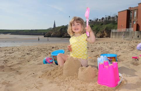 Toddler building sandcastles on a beach.