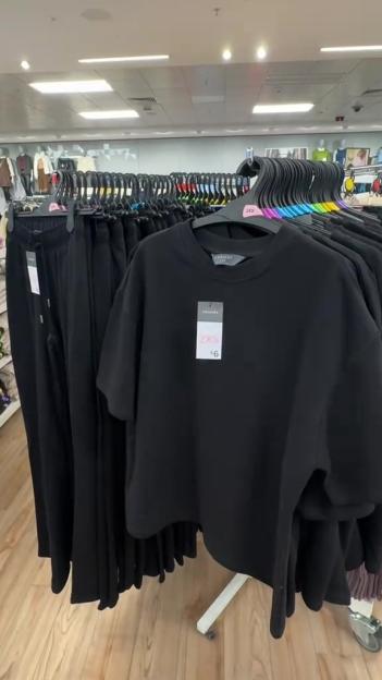 Black t-shirts and sweatpants displayed on racks in a Primark store.