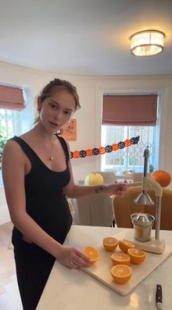 A woman in a black top standing in a kitchen, preparing to juice oranges with a manual juicer.