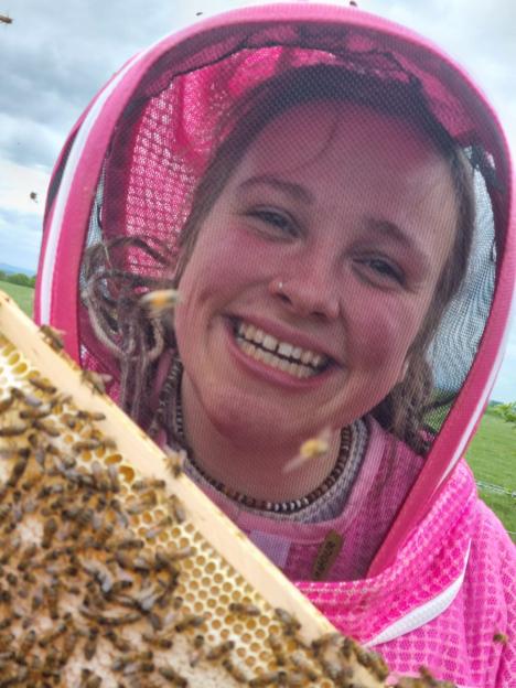 Smiling beekeeper holding a honeycomb frame.