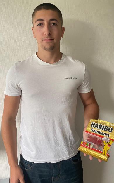 A young man holding a package of Haribo Goldbears with six gummy bears stuck together.