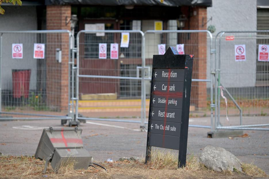 Sign outside The Bell Hotel with "Car park" and "Restaurant" crossed out in red paint, implying a change of use for asylum seekers.