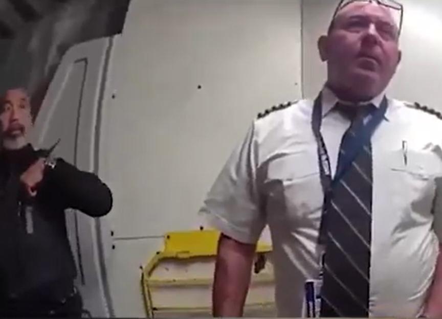 Police officer escorting a pilot from a cockpit.