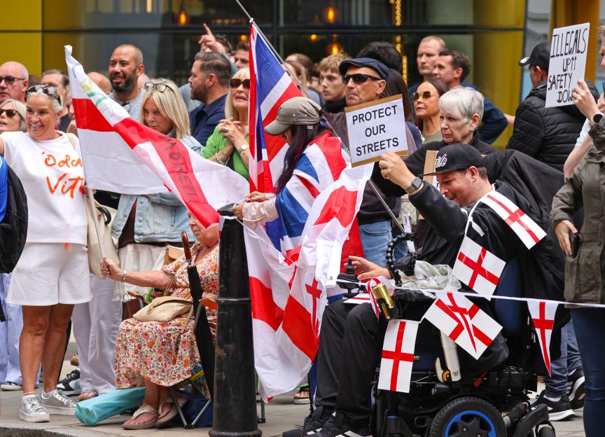 Protestors holding signs and English flags at a demonstration.