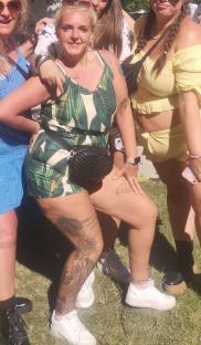 Woman in tropical print shorts and top with tattoos on her legs.