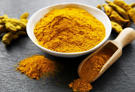 Turmeric powder in a bowl and scoop, with turmeric roots.