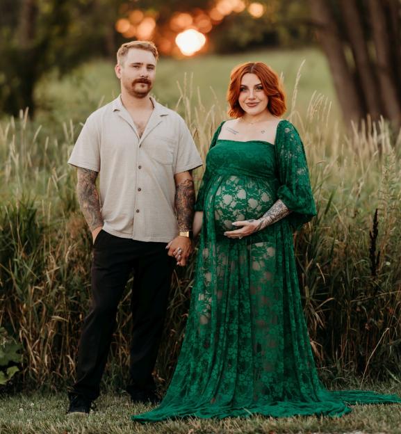Pregnant woman in green dress holding hands with her husband.