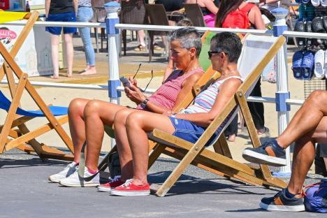 Two women relaxing in deck chairs on a sunny seafront.