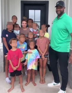 A large family stands on their porch; the parents are flanked by their many children.