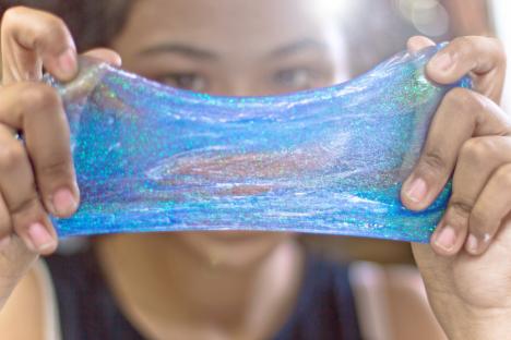 Teenage girl stretching blue glitter slime.