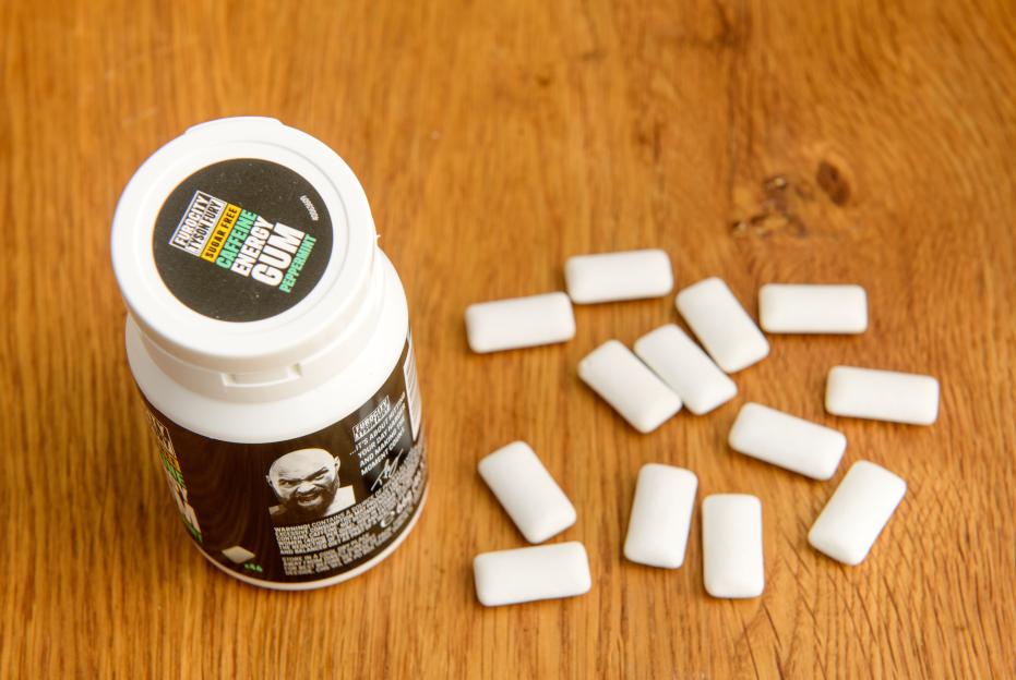 Bottle of Tyson Fury endorsed caffeine energy gum and several pieces of gum on a wooden surface.