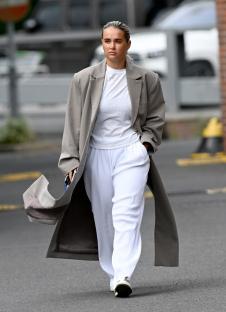 Woman walking down the street wearing a long gray coat and white pants.