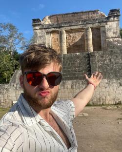 Man in sunglasses gesturing toward Mayan ruins.