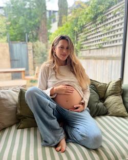 Pregnant woman sitting on a couch, holding her belly.