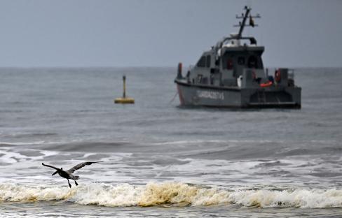 Pelican flying over ocean waves near a Coast Guard boat.