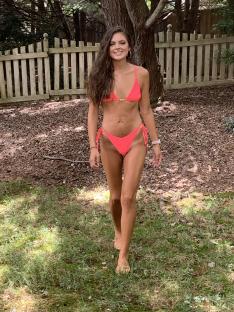Woman in coral bikini walking barefoot on grass.