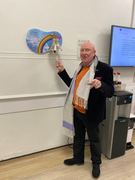 Patrick Howard ringing a bell on a rainbow-themed plaque, celebrating the completion of his cancer treatment.