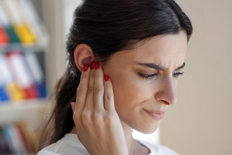 Woman holding her ear, experiencing tinnitus.