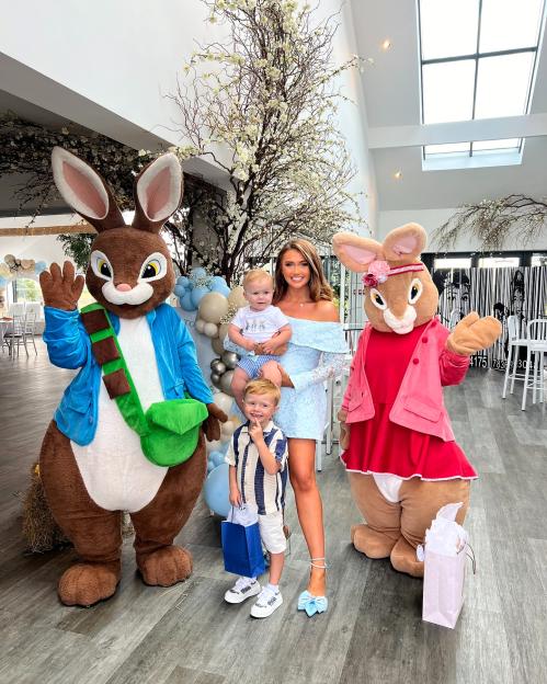 A woman and her two sons pose with Peter Rabbit and Flopsy Bunny mascots at a birthday party.