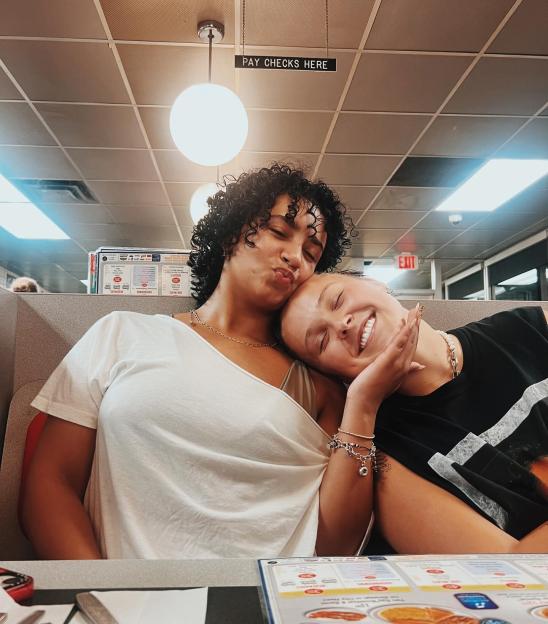 Two women cuddling in a diner booth.