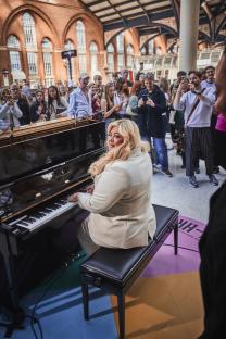 Gemma Collins playing a piano with a crowd watching.