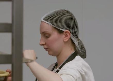 A woman wearing a hairnet prepares food.