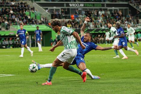 Abdessamad Ezzalzouli of Real Betis crosses the ball under pressure from Malo Gusto of Chelsea during a soccer match.