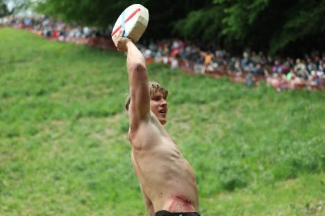 A man holds a cheese wheel aloft after winning a cheese-rolling competition.