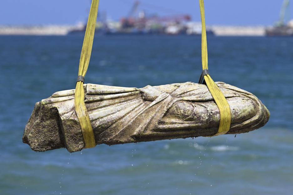 Recovered underwater statue being lifted from the sea by crane.