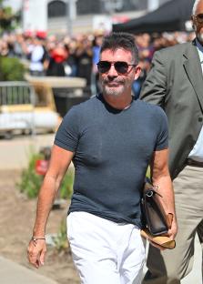 Simon Cowell walking outdoors, carrying a bag.