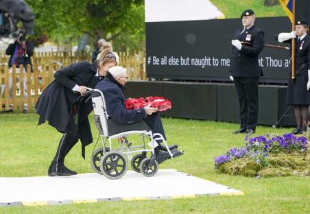A woman assists a veteran in a wheelchair as he lays a wreath at a remembrance service.