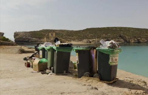 Overfilled trash cans on a beach at night, with an island and calm water in the background.