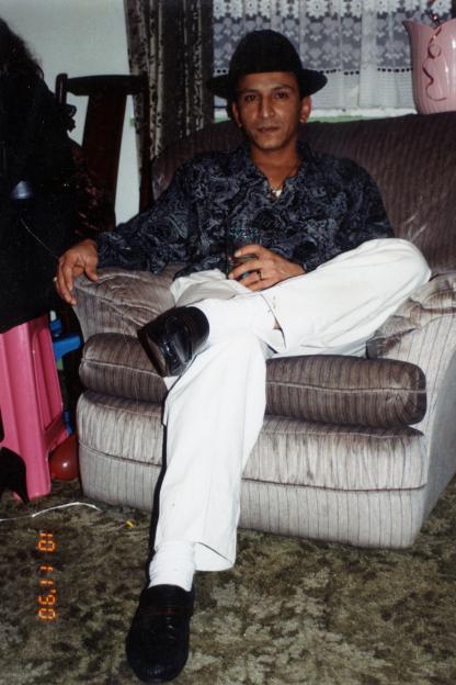 Photo of a man in a hat and patterned shirt sitting on a couch.