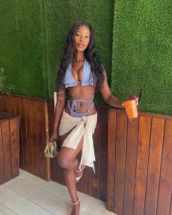 Woman in a light blue bikini and beige sarong holding a drink.
