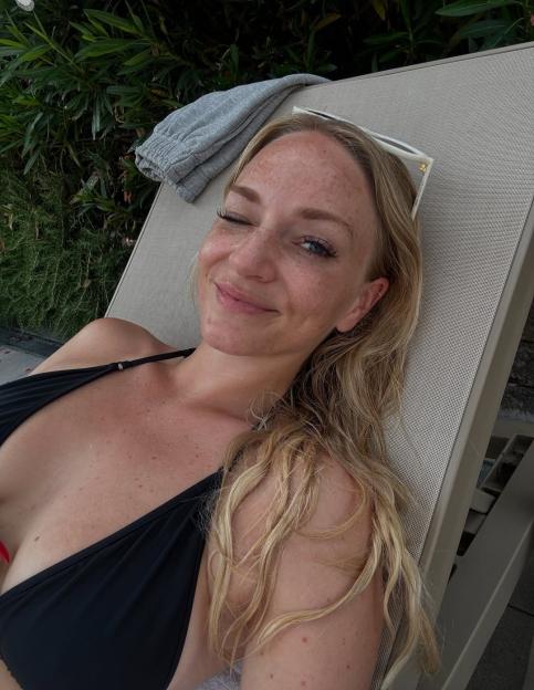 Woman in a black bikini winking at the camera while lying on a lounge chair.